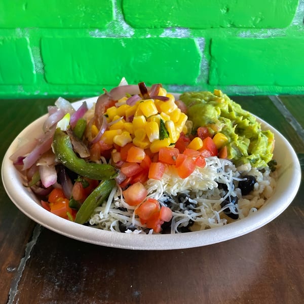 Colorful burrito bowl with rice, black beans, cheese, corn, tomatoes, guacamole, and grilled vegetables.