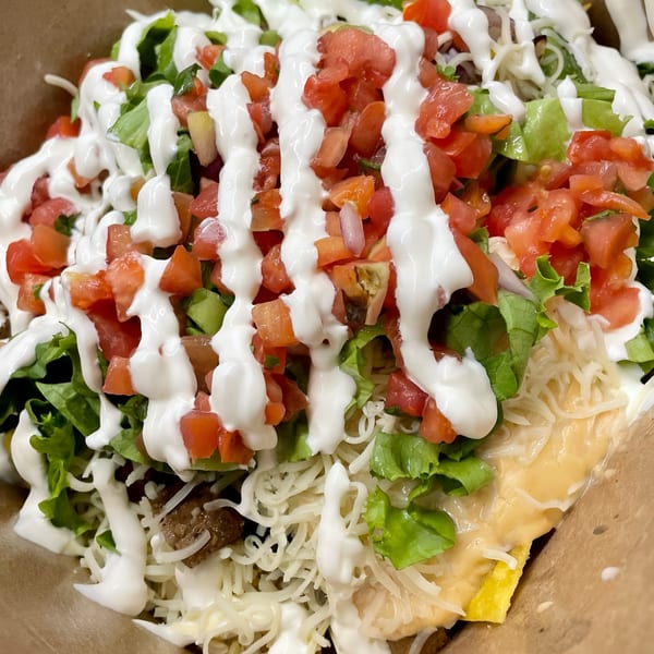 A vibrant taco salad with lettuce, tomatoes, shredded cheese, and sour cream in a paper bowl.