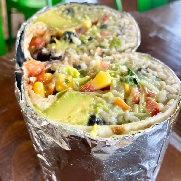Freshly cut burrito wrapped in foil, showcasing vibrant rice, black beans, corn, tomato, and avocado fillings.