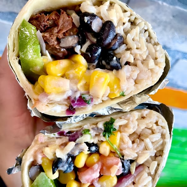 Burrito cut in half, showing vibrant fillings: shredded meat, black beans, rice, corn, and creamy sauce.